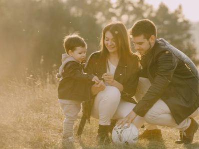 A cheerful family bonding outdoors with a soccer ball, enjoying a sunny day in the grass.